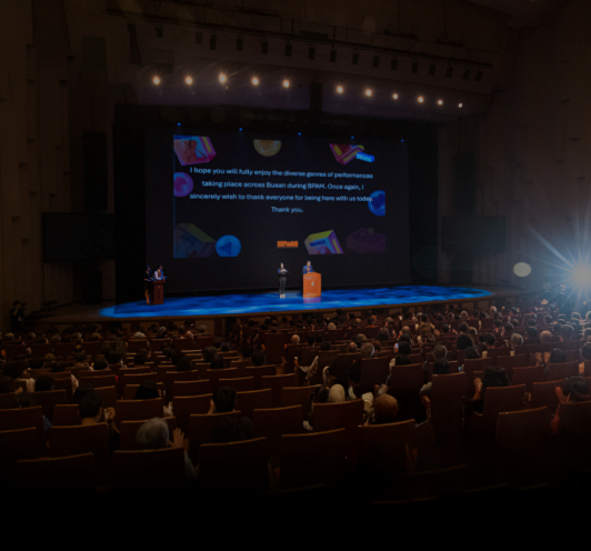 강연장에서 사람들이 무대 위 화면을 보고 있는 모습