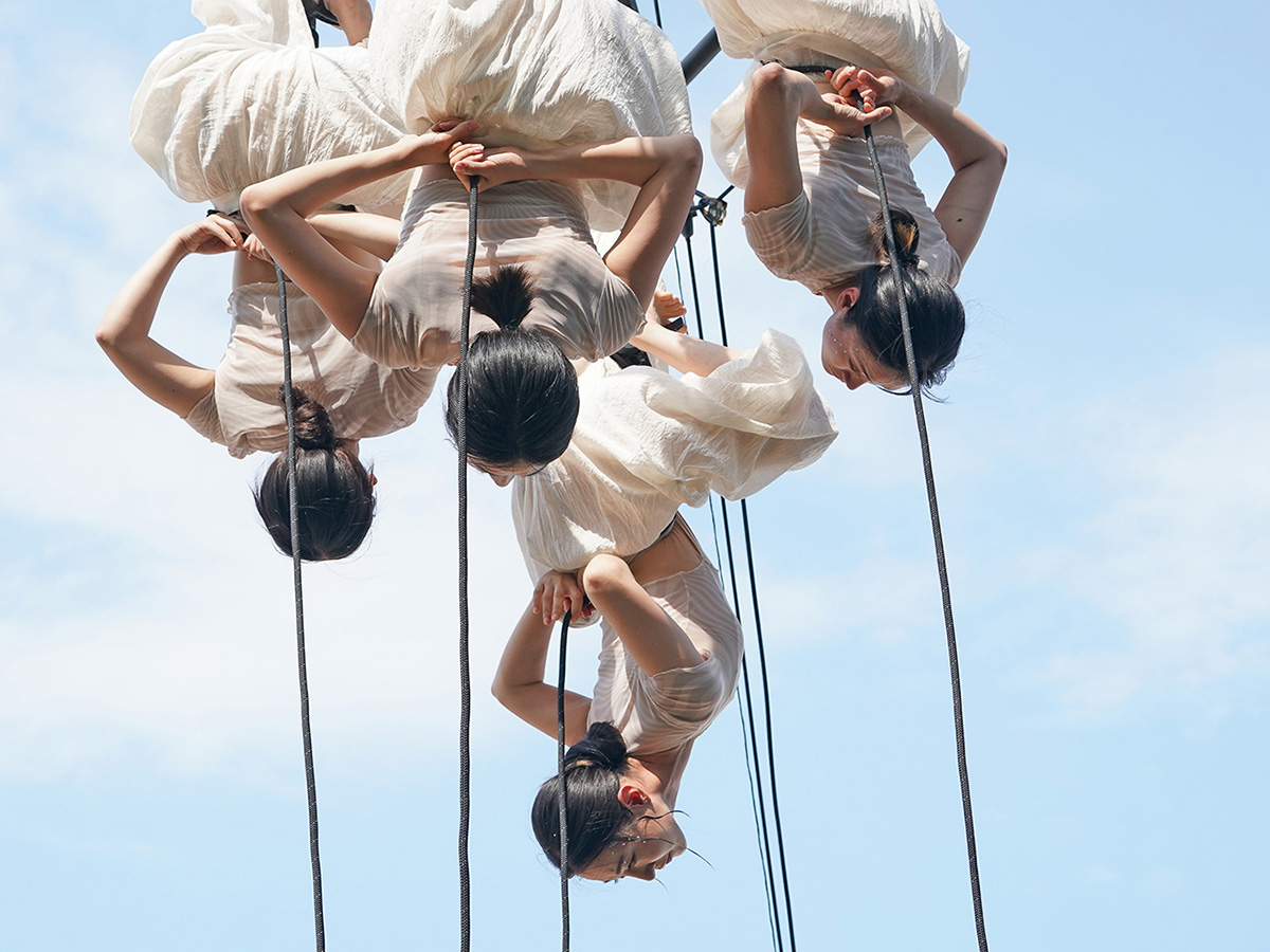 푸른 하늘을 배경으로 공중에서 로프에 매달려 공연하는 무용수들