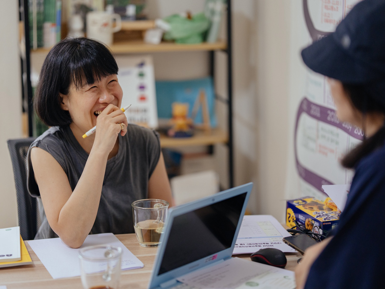 책상에 앉아 활짝 웃는 여성과 그를 마주보는 사람