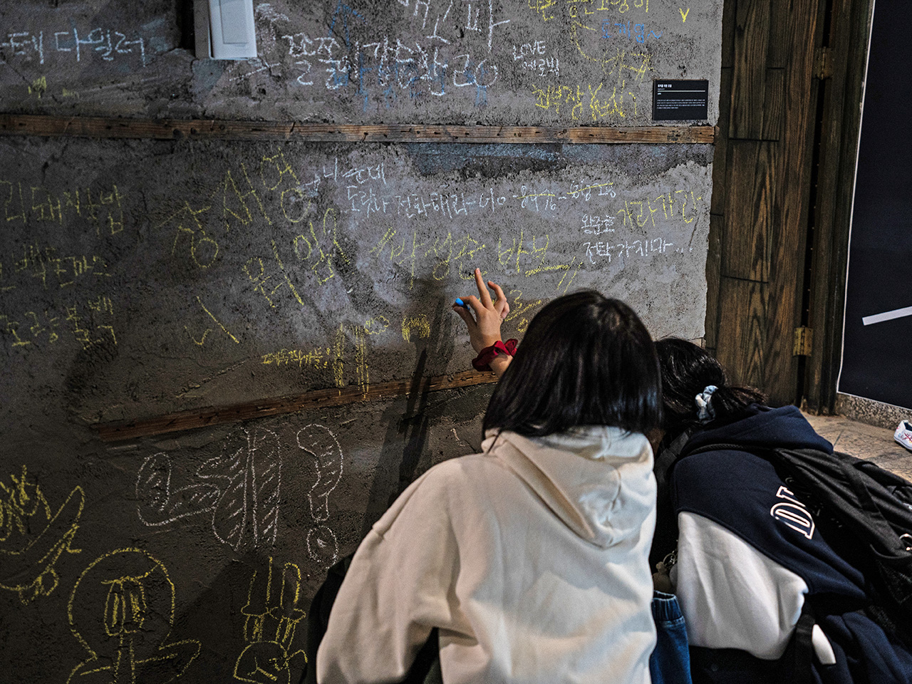 시멘트 벽에 분필로 낙서하고 있는 두 사람의 뒷모습