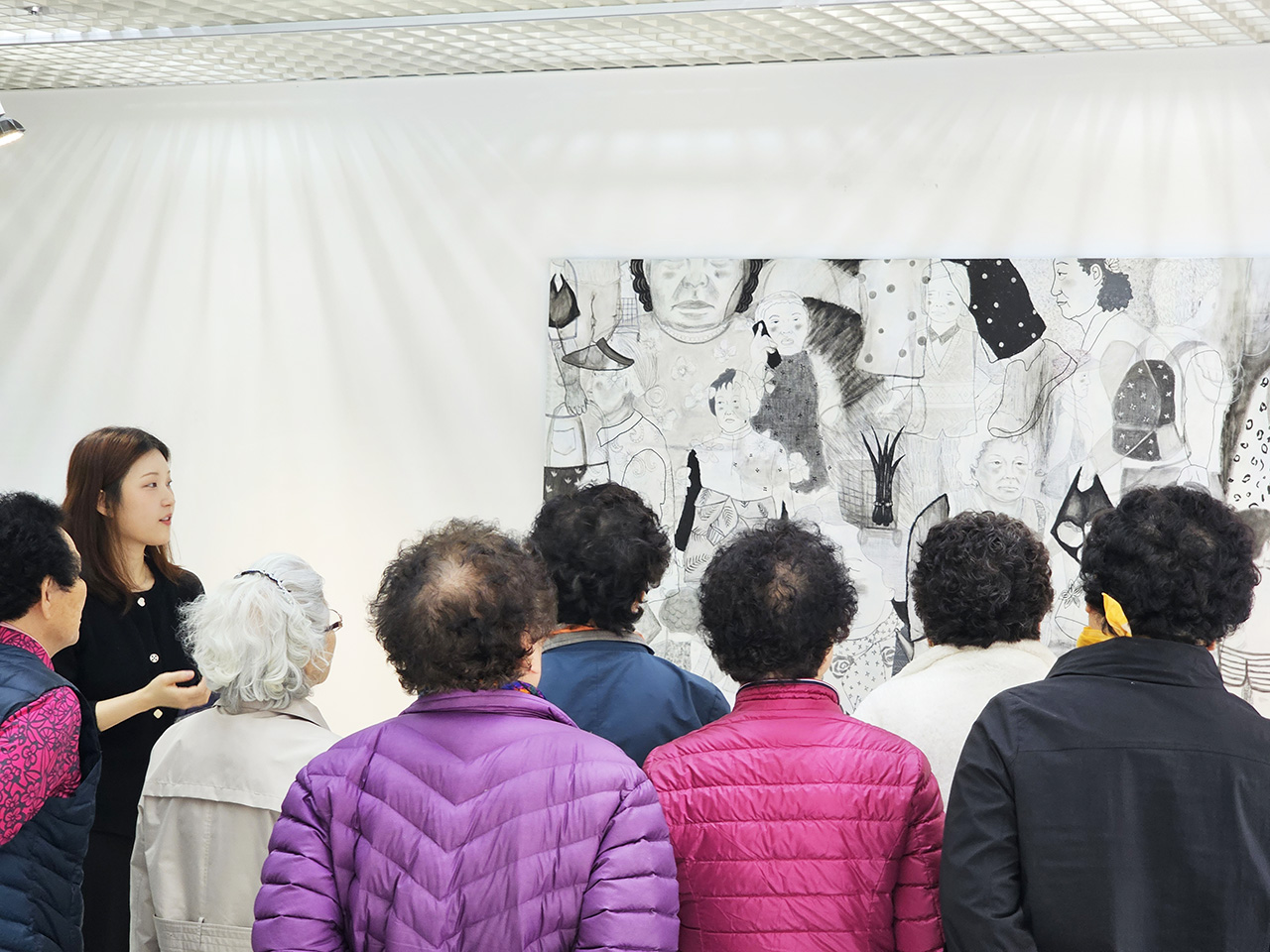 여성 작가가 여러 명의 관람객에게 자신의 작품을 설명하고 있는 모습